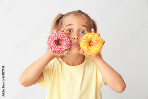 Funny little girl with donuts on light background