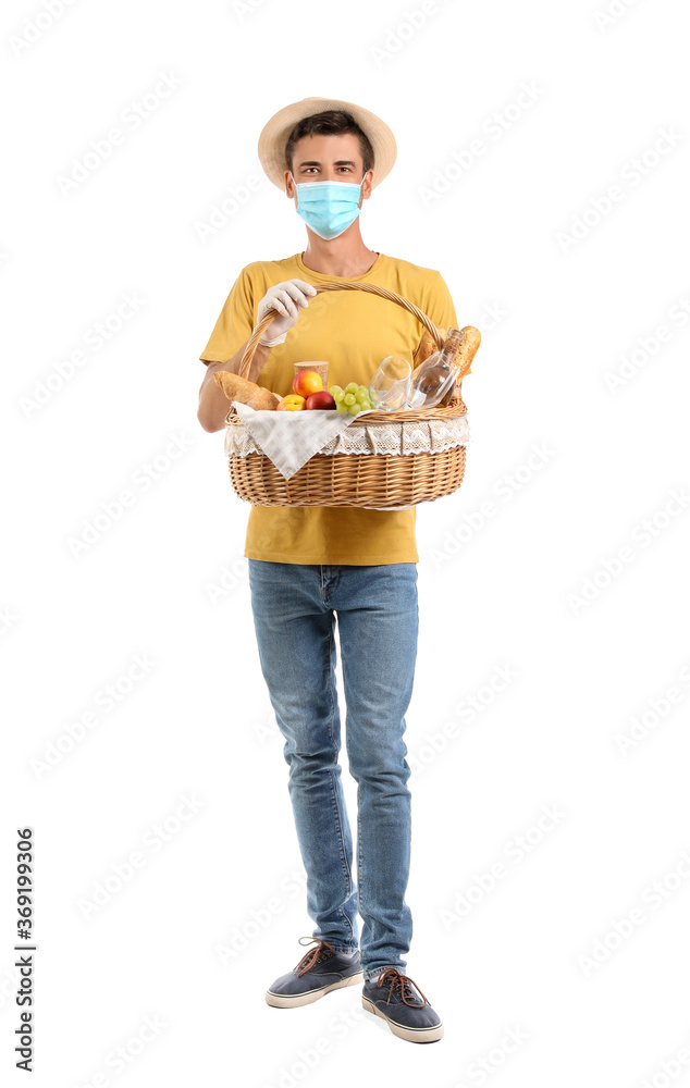 Young man with protective mask and food for picnic in basket on white background Young man with protective mask and food for picnic in basket on white background