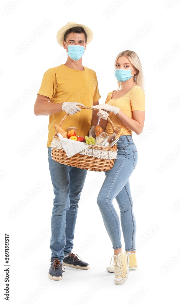 Young couple with protective masks and food for picnic in basket on white background Young couple with protective masks and food for picnic in basket on white background
