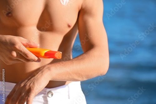 Handsome young man applying sunscreen cream on sea beach, closeup