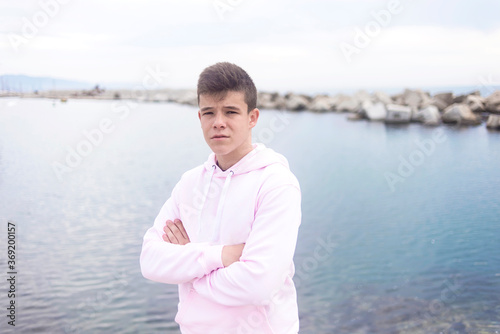 Young teenager male with crossing arms standing on promenade while looking at camera