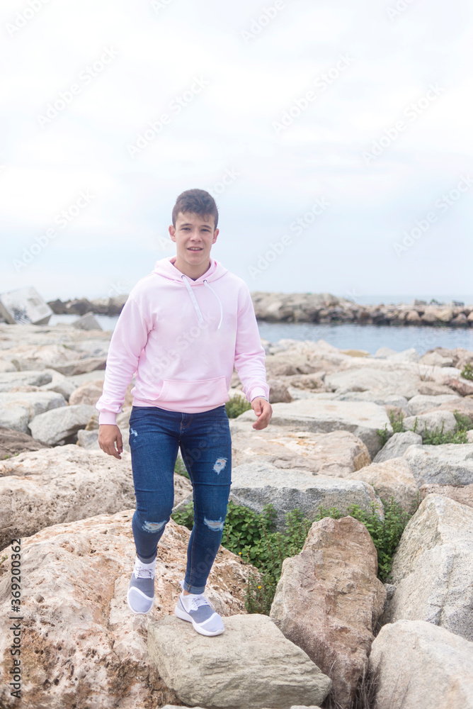 Young teenager male walking over rocks breakwaters while looking at camera