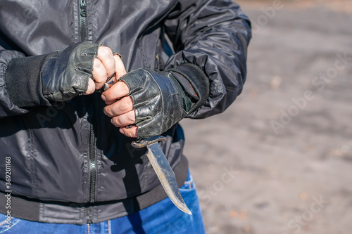 knife in the hands of a bandit in a black jacket and leather gloves, who stands on the street during the day