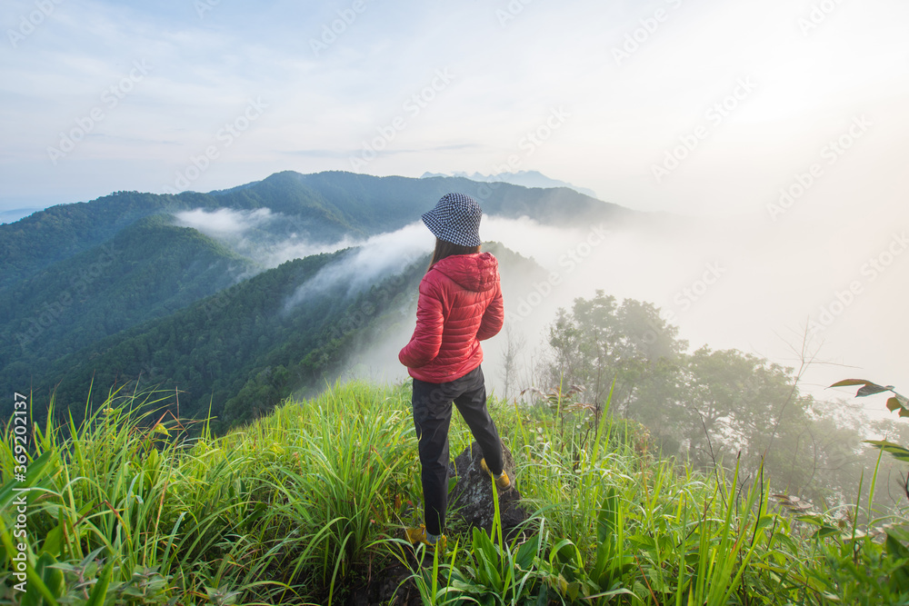 Naklejka premium rear of happy woman stand on top mountain looking view with mist and cloud at morning light Soft focus.