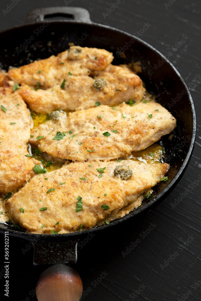 Homemade Italian Chicken Piccata in a cast iron pan on a black background, side view.