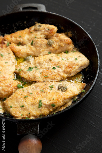 Homemade Italian Chicken Piccata in a cast iron pan on a black background, side view.