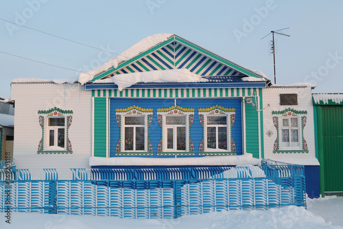 Wooden rural house with richly decorated traditional national carved windows in russian village (Ulyanovsk region, Russia). Russian folk style in wooden architecture. Building facade. Snow winter photo