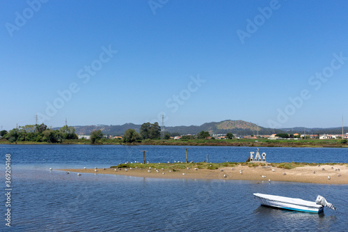 Fão / Esposende / Portugal -  July 29, 2020: A small boat moored in the Cavado River estuary on a sunny day. Word FAO made of stone concrete letters. photo