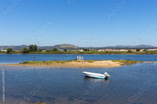 Fão / Esposende / Portugal -  July 29, 2020: A small boat moored in the Cavado River estuary on a sunny day. Word FAO made of stone concrete letters.