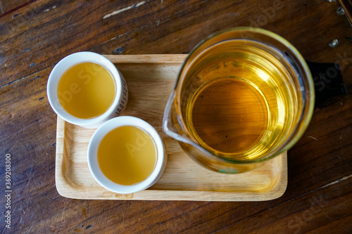 simple still life with green tea, flat lay. Chinese tea in a transparent teapot and two traditional white Asian mugs. On a wooden table and a tray 