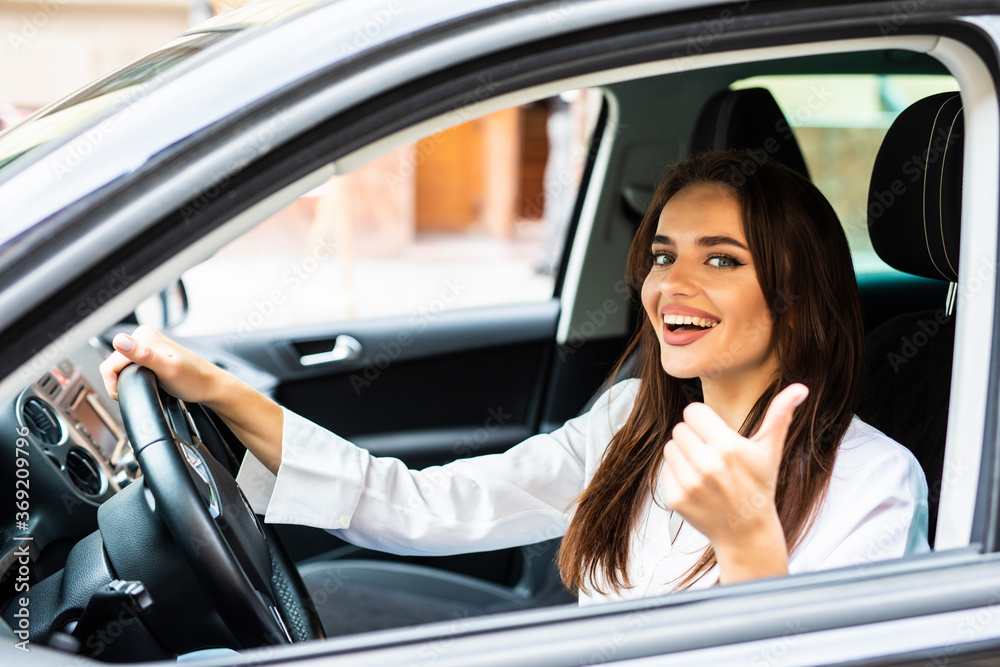 Portrait of a beautiful young woman with thumbs up in her new car