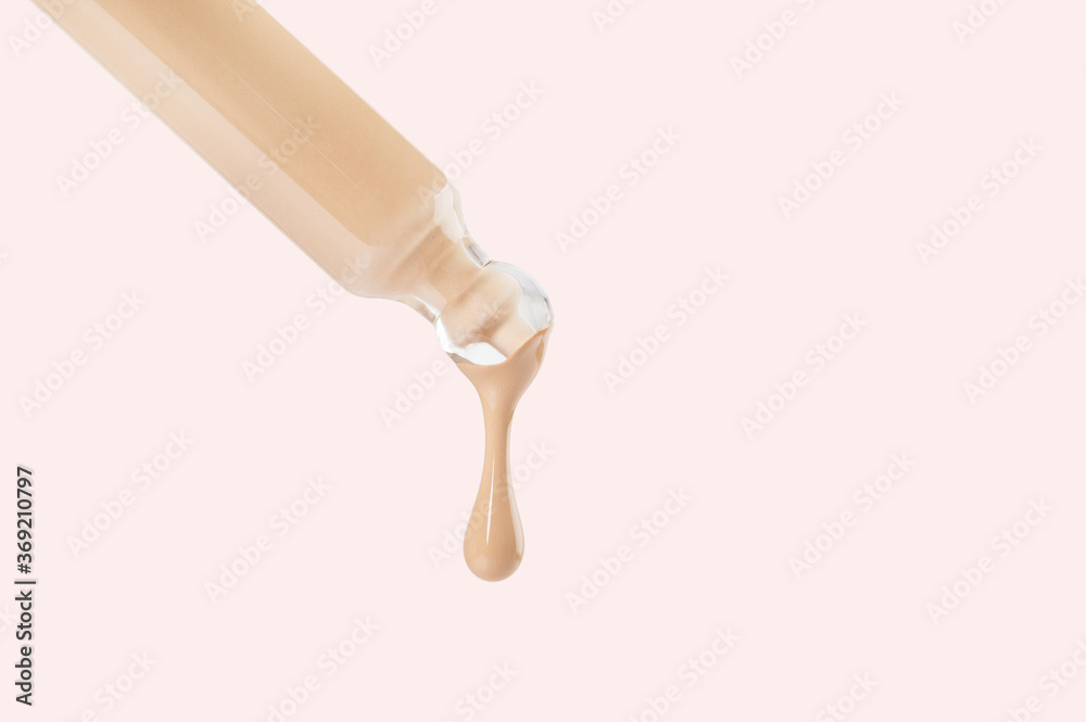 Glass pipette with flowing matte nude foundation drop white background. Sample of cosmetic beauty makeup product. Liquid tint, fluid, beige concealer for contouring, skin tone correction. Copy space