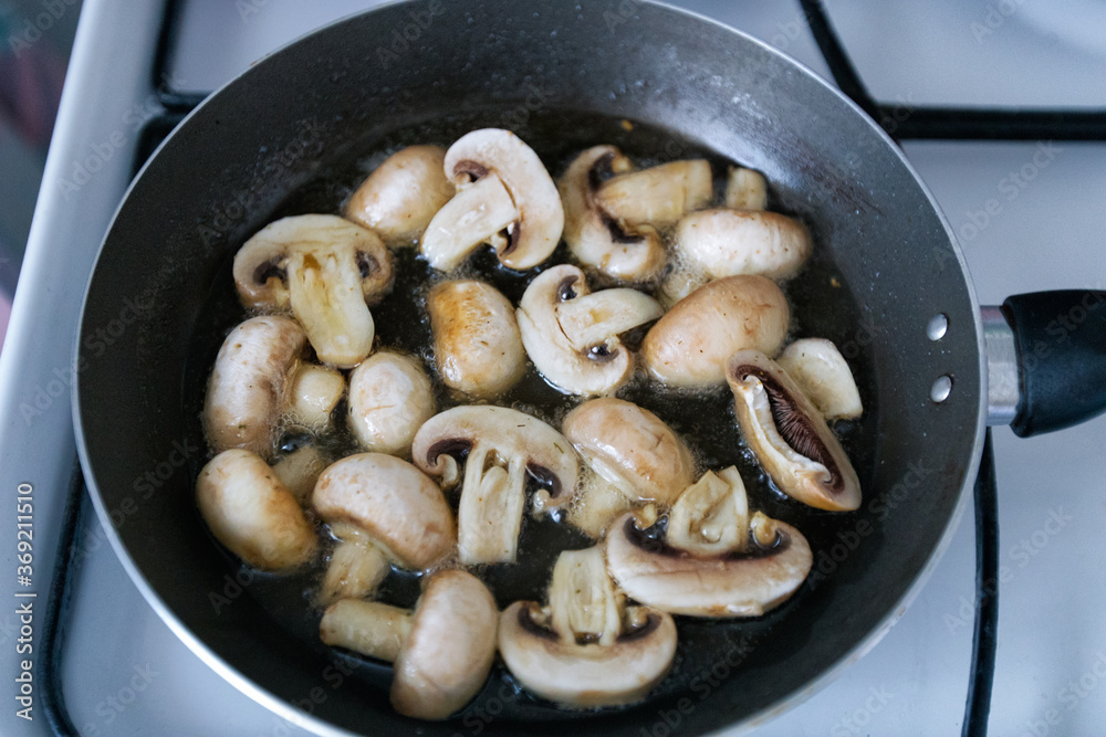 Sauteed in olive oil small champignons with chopped garlic. Mushroom cooking in frying pan top view. Homemade food.