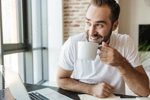 Image of man drinking coffee and using laptop while sitting at table