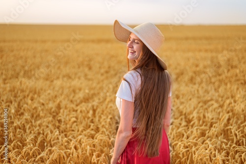 Beautiful young woman in hat walking on field of ripe wheat