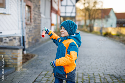 Little school kid boy of elementary class walking to school on cold winter day. Happy child having fun on a city street. Student with backpack in colorful winter clothes holding things for project