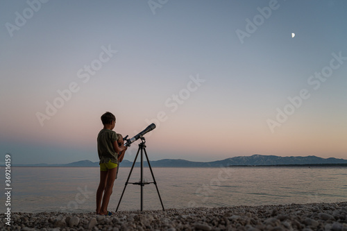 Brothers standing on beautiful pebble beach looking to the stars with a telescope