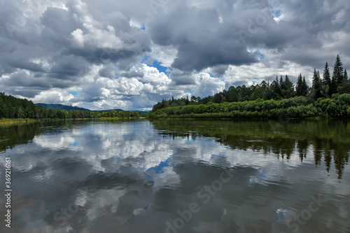 Fototapeta Naklejka Na Ścianę i Meble -  A natural landscape with clouds reflecting on the surface of a calm river with green forest on its banks in Siberia