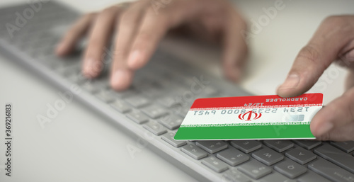 Man pays online with plastic bank card with printed flag of Iran. Fictional numbers