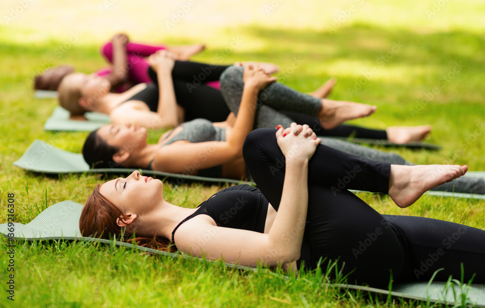 Calm young women lying on yoga mats and stretching their legs at park, blank space