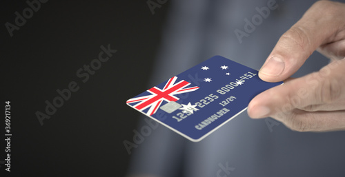 Man offers plastic bank card with printed flag of Australia. Fictional numbers