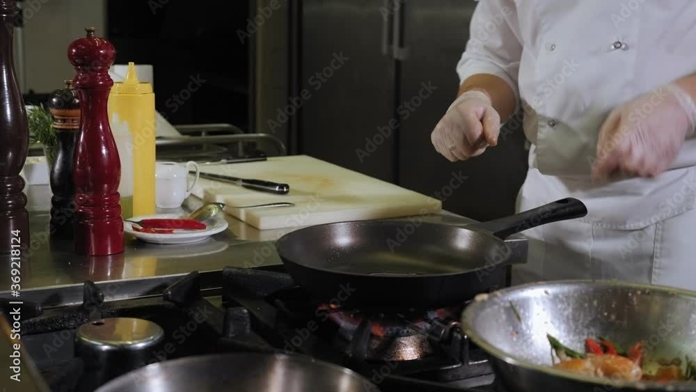 Close-up of a male chef pours oil on a frying pan that stands on the stove in a professional kitchen in a restaurant, the process of cooking in a restaurant. Close-up of a male chef pours oil on a frying pan that stands on the stove in a professional kitchen in a restaurant, the process of cooking in a restaurant.