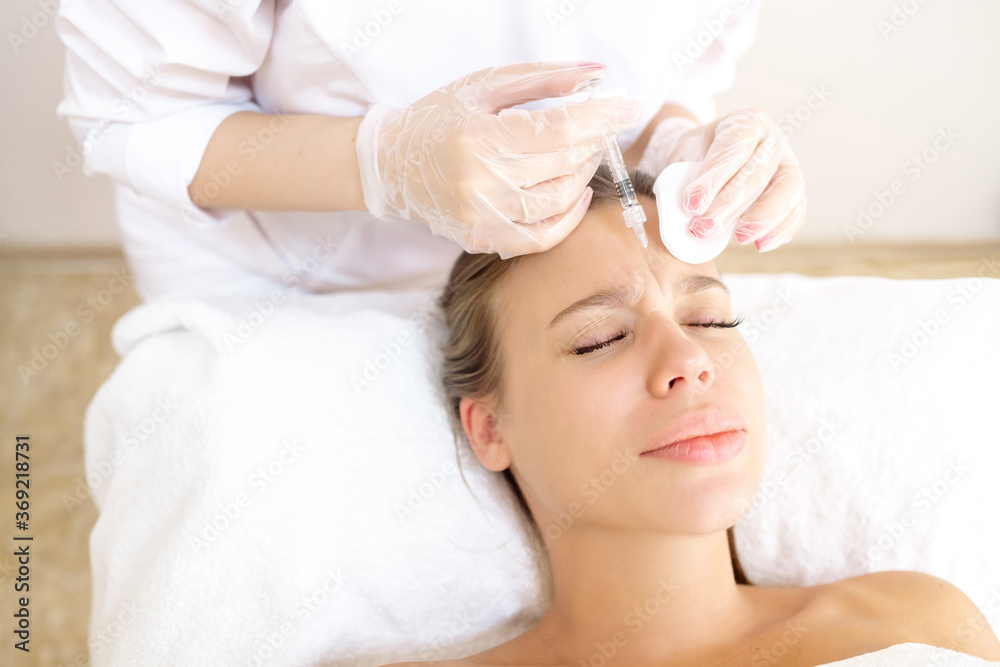 The beautician makes the patient wrinkle correction with botox in the forehead and between the eyebrows