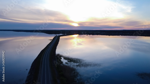 A road passing in the middle of the lake. Sunset over the water. Reflection of the sky in the water