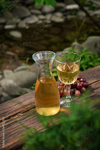 Carafe with white wine on a wooden table. With a glass and a bunch of grapes
