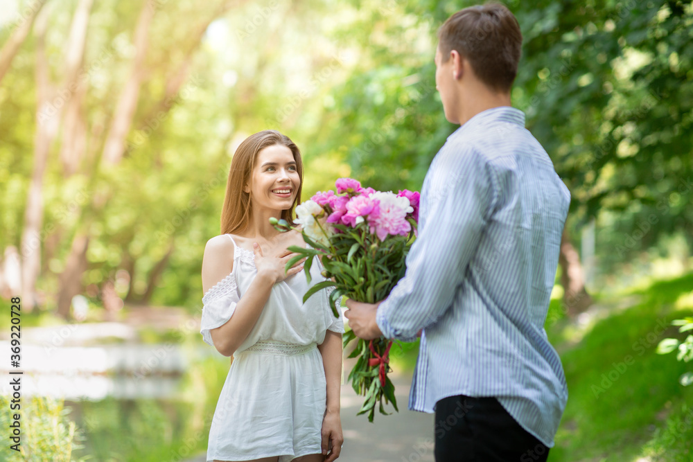 Affectionate young man surprising his girlfriend with bouquet of flowers at park