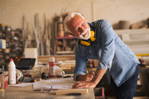 Nice elderly craftsman looking behind his back and smiling