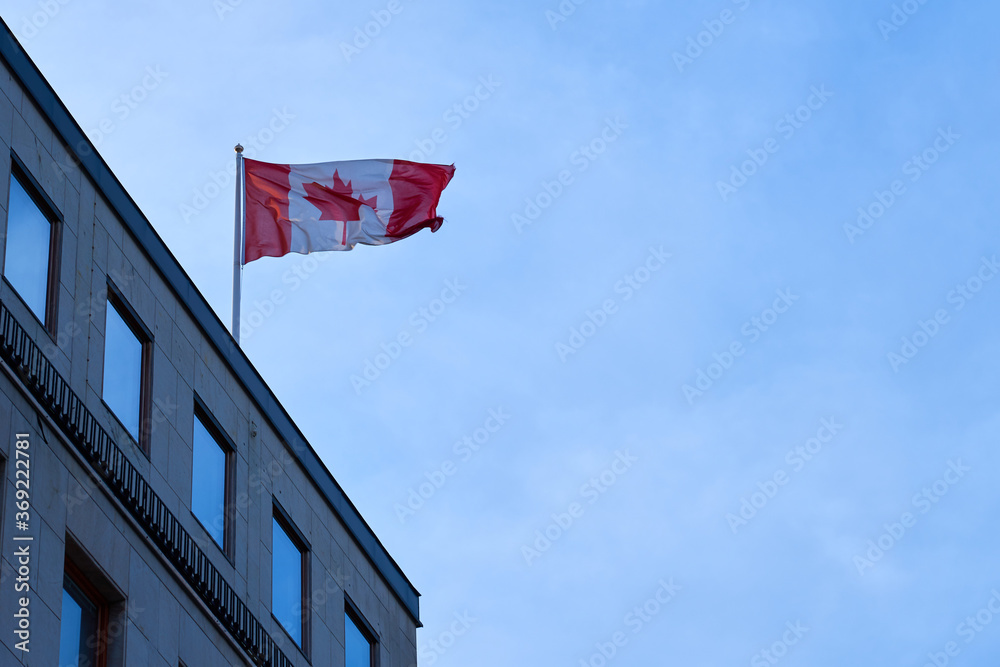 A flag of Canada on a roof of a building against a cloudy sky. Copy space.