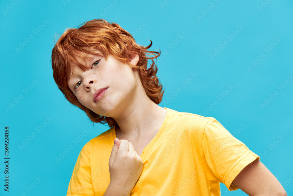 A boy with red hair in a yellow T-shirt leaned to the side against A boy with red hair in a yellow T-shirt leaned to the side against