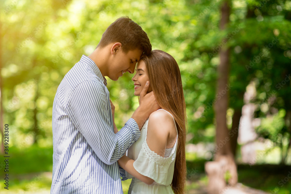 Romantic relationship. Handsome young guy and his girlfriend cuddling in park on summer day Romantic relationship. Handsome young guy and his girlfriend cuddling in park on summer day