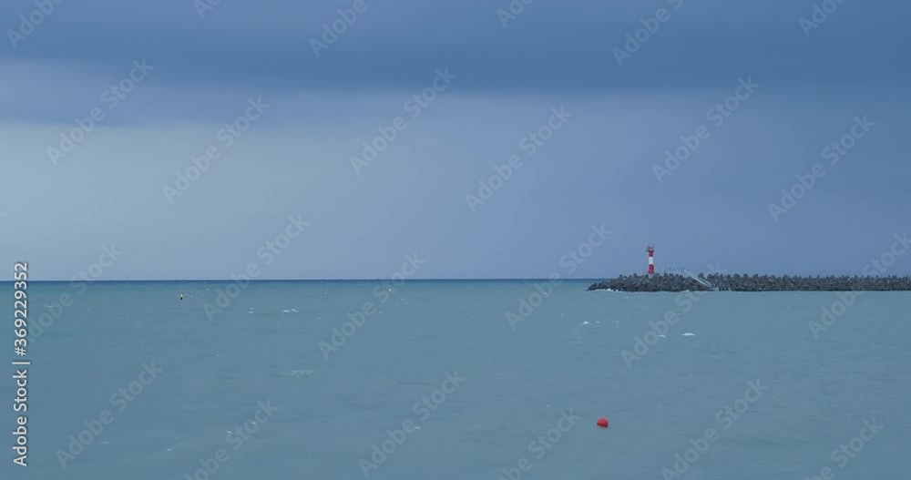 Seagulls and cormorants sit on breakwater. Lighthouse on stormy sky background. Port of Sochi, Russia. Seagulls and cormorants sit on breakwater. Lighthouse on stormy sky background. Port of Sochi, Russia.