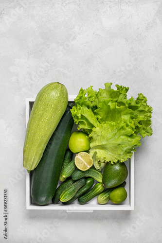 Variety of organic green raw vegetables and fruits: zucchini, cucumber. avacado, apple, lime in a white box on a gray background. Healthy lifestyle. Balanced diet. Green detox