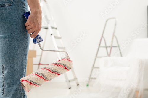 Close-up of unrecognizable woman in jeans holding paint roll in room with stepladders