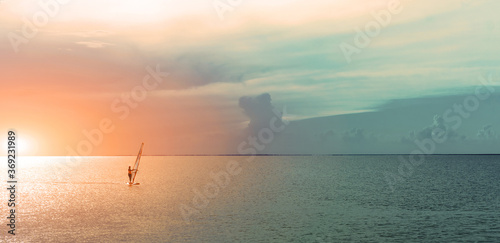 silhouette windsurfer sailing on windsurf board on sea at a beautiful sunset sky on background. Healthy active lfestyle, hobby, summer fun adventure.