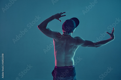Guy breakdancer in cap dance hip-hop in neon blue light. Dance school poster. View from the back