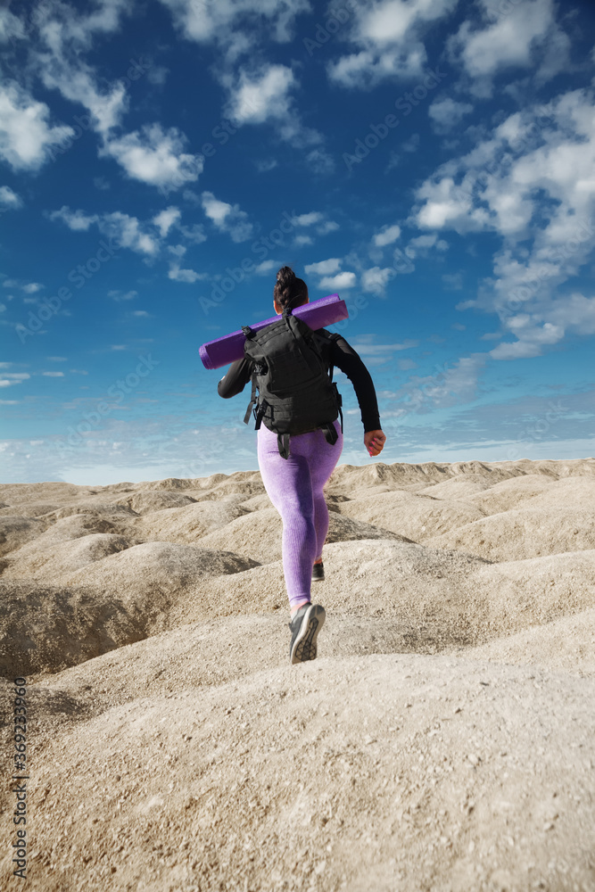woman solo tourist running in jump, rear view on hill area in sportswear and with backpack looking into distance on sunny day, concept of healthy lifestyle, sports, overcoming obstacles