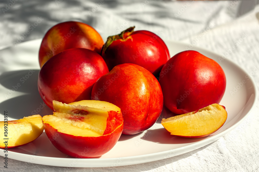 Red ripe organic nectarine fruits on the white plate on nature background. Summertime healthy eating concept. Fruit antioxidant. Selective focus Red ripe organic nectarine fruits on the white plate on nature background. Summertime healthy eating concept. Fruit antioxidant. Selective focus