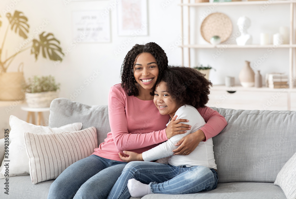 Happy Black Mother Embracing Her Cute Little Daughter On Couch At Home
