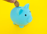 A hand putting a coin into a piggy bank. moneybox on a yellow background