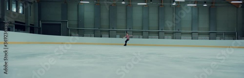 Professional teenager male ice figure skater practicing on the indoor rink. Shot on RED cinema camera with 2x Anamorphic lens, 75 FPS slow motion photo