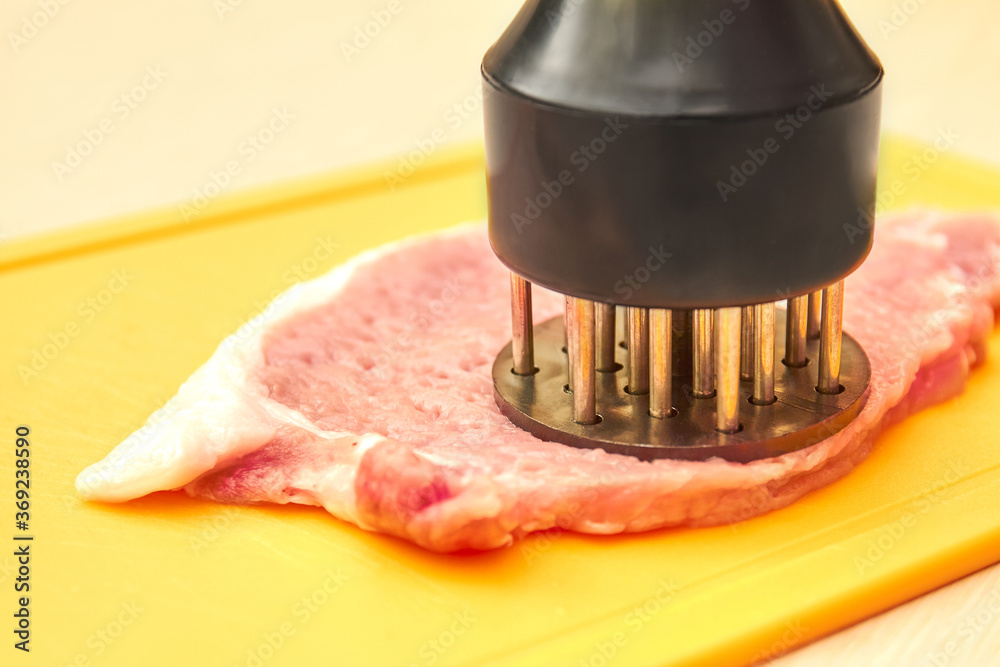 Piece of pork and meat tenderizer on cutting board Piece of pork and meat tenderizer on cutting board