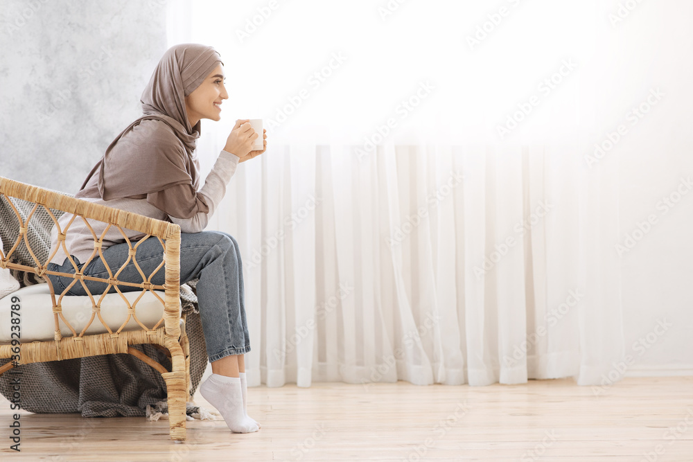Relaxed Morning. Arab Woman Resting In Wicker Chair At Home With Coffee - obrazy, fototapety, plakaty 