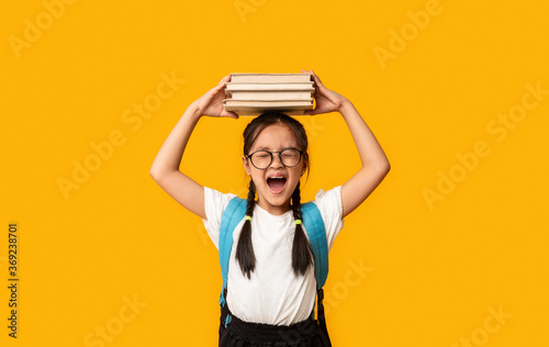 Discontented Japanese Girl Shouting Holding Books On Head, Yellow Background