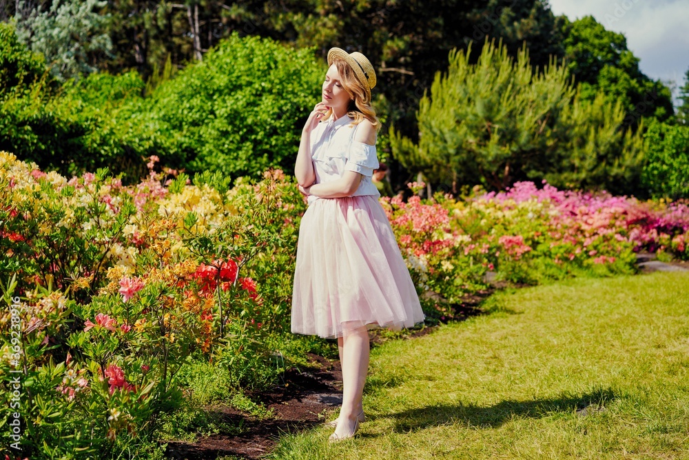 Gorgeous young  woman in hat posing in a blooming garden. Beautiful girl dressed in pink skirt and white blouse. Sensual woman with perfect skin and with natural makeup. fashion and style concept.