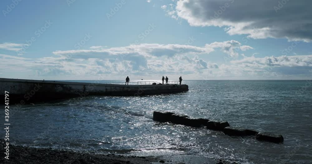 Silhouettes of people taking photos of black sea on pier. Tranquil sea surf at daylight, Sochi, Russia. Silhouettes of people taking photos of black sea on pier. Tranquil sea surf at daylight, Sochi, Russia.