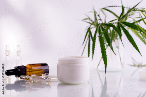Natural cosmetics with cannabis oil. Mockup with a White clean jar with cosmetics cream and green leaves of hemp.